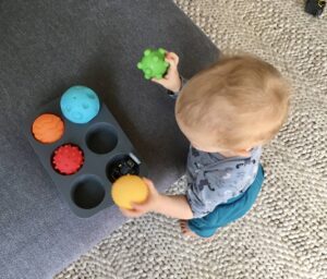 Ein Baby räumt Bälle in Muffinformen