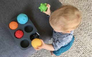 Ein Baby räumt Bälle in Muffinformen